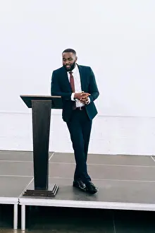 Formal Wear Prints: handsome african american businessman leaning on podium tribune and talking during seminar in conference hall