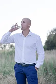 Mature Men Prints: handsome bald man in white shirt and blue pants with glass of white wine in the field
