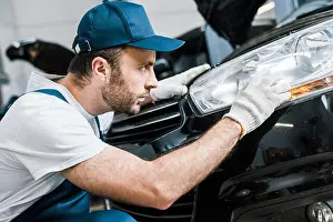 Professional Occupation Prints: handsome bearded auto mechanic in cap looking at tail light in black car
