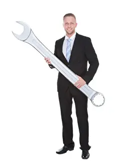Wrench Prints: Handsome bearded businessman in a smart suit holding a large metal spanner in his hands conceptual of problem solving
