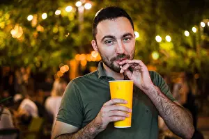 Wineglass Prints: Handsome Bearded European Man Drinking coctail or beer at outdoor Street Cafe or night party in park