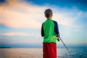 Angling Prints: handsome blond boy angling fish by the Mediterranean sea in the evening