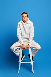 Sneaker Prints: Handsome man wearing white sweatshirt and sweatpants sitting on white chair over blue studio background