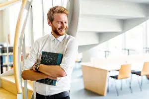 Bookshelf Prints: Handsome smart guy reading a book in a library