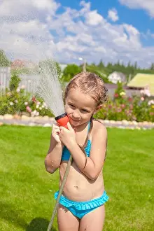 Happy adorable little girl pouring water from a hose and laughing