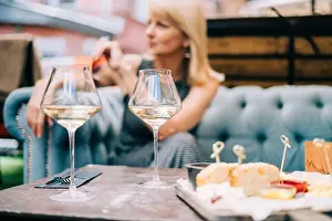 Tasting Prints: Happy adult woman sitting on couch in bar outdoors with wine glasses and blurry restaurant background scene