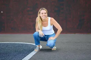 Tanktop Prints: Happy blonde woman in casual white tank top and jeans squatting on pavement outdoors