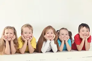 Five happy children (three girls and two boys) pose in white studio