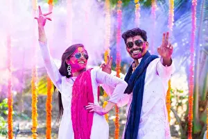 Holi Prints: Happy couple dancing during holi festival celebration with colorful face and dress at ceremony - concept refreshment
