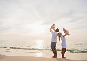 Mid Adult Women Prints: Happy family with two baby girls (2-5 months) at beach in sunlight
