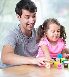 Preschooler Prints: Happy father and daughter playing with building blocks at table in house