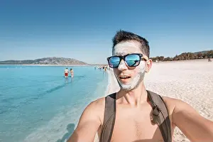 Applying Prints: Happy and funny young male tourist in sunglasses takes a selfie at a therapeutic mud resort of Salda lake in Turkey