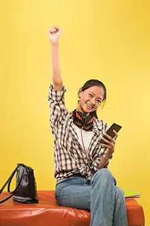 Favorite Prints: happy girl with raised fist up and looking at camera while holding and using cellphone while sitting