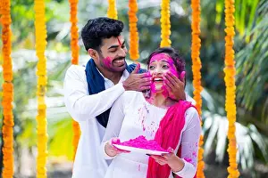 Applying Prints: Happy indian young husband applying holi colors to wife face by holding holi powder plate during celebration holi
