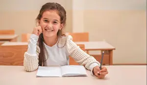 Preteen Prints: A happy kid girl sitting at a school desk in the classroom