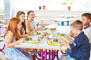 Junior Prints: Happy kids having meal with cutlery while sitting together at table in school canteen