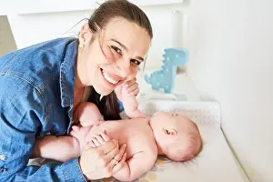 Diaper Prints: Happy mother lovingly holds her baby by the hands while caring for it on the changing table
