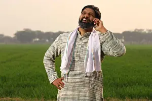 35 39 Years Prints: Happy rural Indian farmer man using his mobile phone he is on a voice call on his smart phone while standing in a