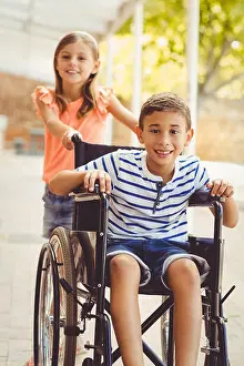 Schoolboy Prints: Happy schoolgirl pushing a boy on wheelchair
