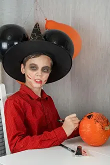 Happy teen boy in costume drawing a pumpkin for the Halloween celebration