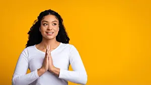 Mindfulness Prints: Happy Woman With Dark Skin Smiles While Clasping Hands Together in Front of Yellow Background