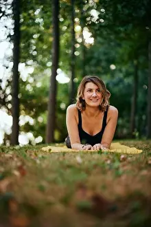 Meditate Prints: A happy woman is lying on her stomach on a yoga mat in the forest and taking a break from exercising