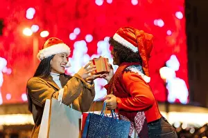 Lgbtq Prints: Two happy women exchanging christmas gifts outdoors at night