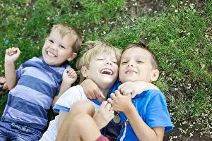 Three happy young boys in summer park. Friends or siblings hugging and laughing while lying down on green grass