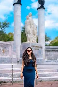 Latina Prints: Happy young Latina woman with long wavy hair and red sunglasses poses smiling in a tight blue dress at Chapultepec