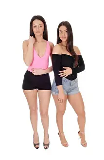 A two happy young slim women standing in the studio in shorts side by side