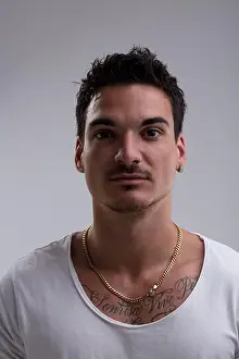 25 29 Years Prints: Headshot of a serious young man with tattoos and a gold chain posing in a studio setting