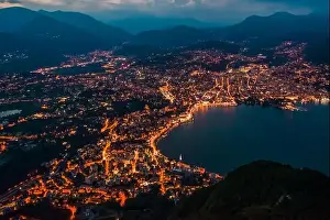 Aerial Cityscape Prints: High angle aerial drone night shot of city street lights by lake in Lugano, Switzerland