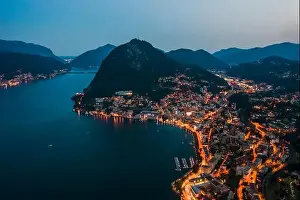 Aerial Cityscape Prints: High angle aerial drone night shot of city street lights by lake monte salvatore in Lugano