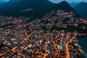 Aerial Cityscape Prints: High angle aerial drone night shot of city street lights by lake monte salvatore in Lugano