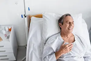 Pills Prints: High angle view of smiling elderly man in patient gown lying on bed in hospital ward