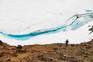 Rugged Landscape Prints: Hiker and dog along Glacial Snowfield with Vibrant Blue Meltwater