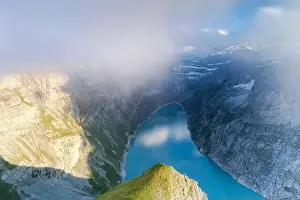 At The Edge Of Prints: Hiker on mountain ridge admiring the foggy sunset over lake Limmernsee