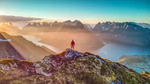 Hiker overlooking amazing mountains lit by midnight sun in Reinebringen, Lofoten, Norway
