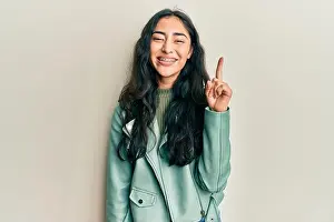 Dental Prints: Hispanic teenager girl with dental braces wearing green leather jacket smiling with an idea or question pointing finger