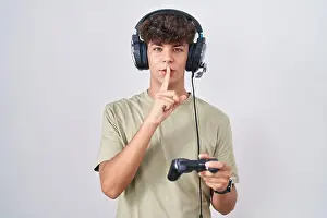 Gamer Prints: Hispanic teenager playing video game holding controller asking to be quiet with finger on lips