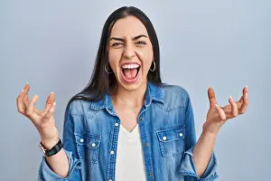 Denim Prints: Hispanic woman standing over blue background celebrating mad and crazy for success with arms raised