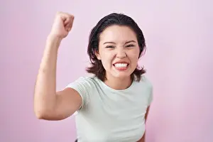 Hispanic young woman standing over pink background angry and mad raising fist frustrated