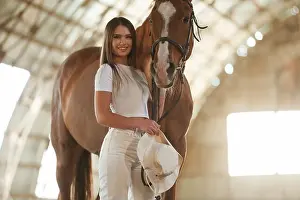 Mare Prints: Holding cowboy hat in hand. Beautiful young woman is with horse indoors