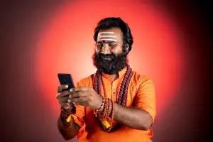 Teller Prints: Holy Indian god man busy using social media on mobile phone at monastery - concept of Mobile astrologer service