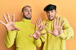 Homosexual gay couple standing together wearing yellow clothes afraid