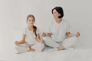 Satisfied Prints: Horizontal shot of happy relaxed brunette mother and daughter pose in lotus pose
