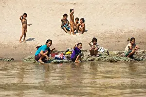 Sisters Prints: Horizontal view of a group of children playing and relaxing on the banks of the Mekong River