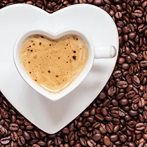 Hot beverage. White coffee cup heart shaped with cappucino latte on roasted beans background