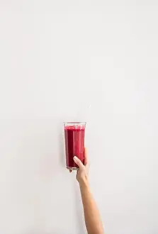 Weight Loss Prints: Human hand holding glass with purple beet pomegranate fresh smoothie with glass straw over white wall background