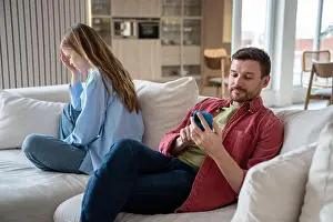 Husband ignoring wife emotions looking at smartphone screen sitting on couch at home